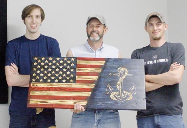 JOHN BAUM, center, was presented with a beautiful patriotic plaque by his sons, Mason, left, and Logan, right, upon his retirement from the U.S. Navy in April.