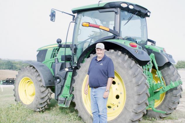 TODD ZIMMERMAN with AKRS Equipment in Auburn stands in front of a modern tractor with many safety devices not available to previous generations.